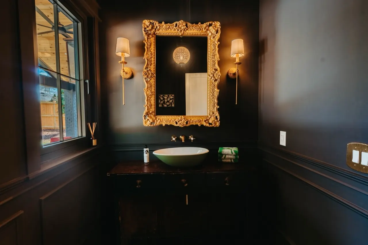 Moody powder room with dark panelling, an ornate gilt mirror and bowl basin — a Cotswold House Co. interior