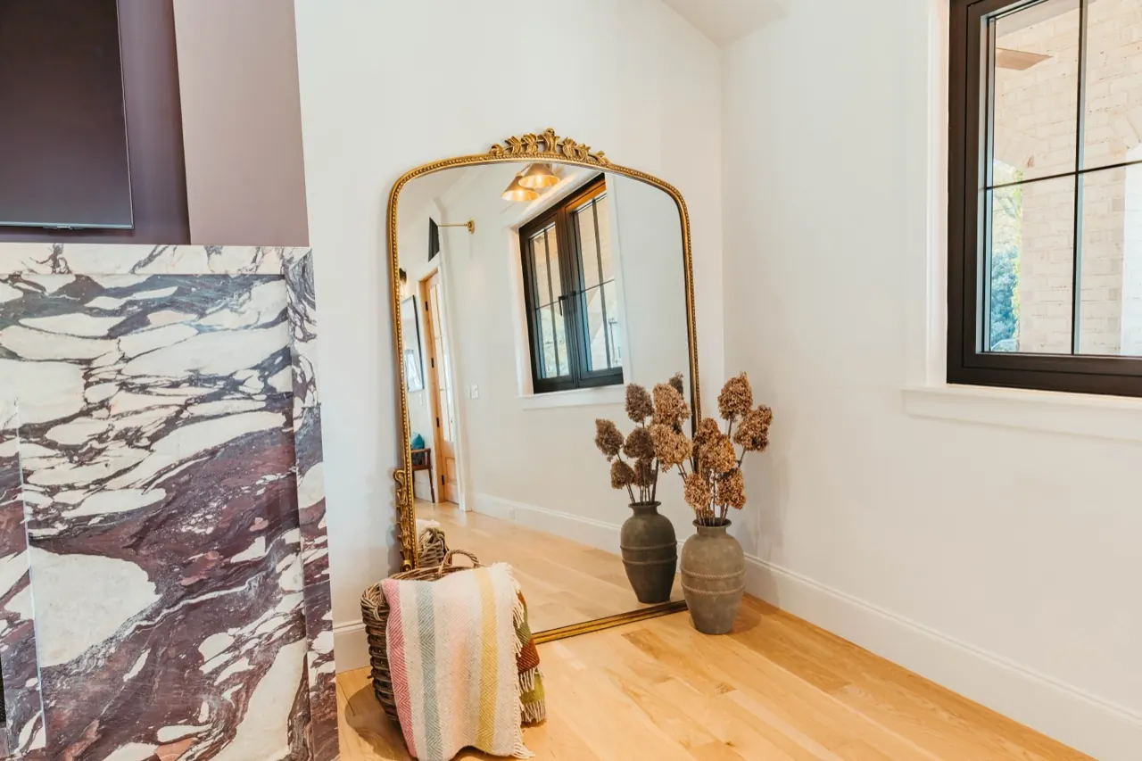 Arched gilt mirror and dried hydrangeas in stone vases at the entry of a Cotswold House Co. interior