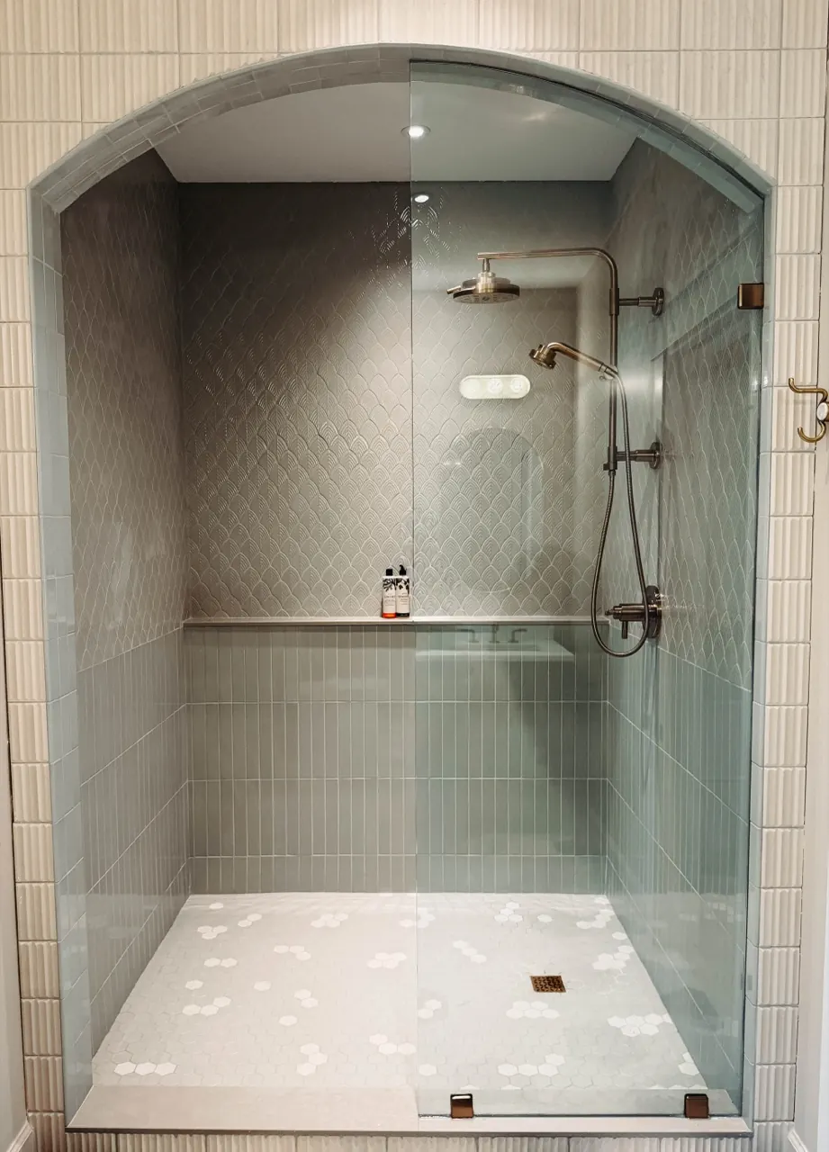 Arched glass shower with hand-laid tile — clean lines, calm, spa-like. Our design language in one detail